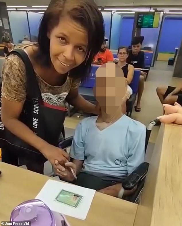 Érika de Souza holds Paulo Braga's hand and a pen while trying to get him to sign a loan document at a bank branch in Rio de Janeiro.  De Souza, a mother of six, said to him: 'Man, are you listening?  You have to sign it.  I can't sign for you'