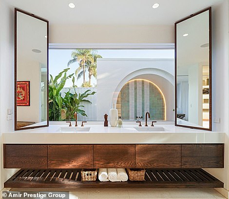 Flowing white curtains around the bed add a touch of elegance, while the bathroom's double vanity has a glass backsplash that overlooks the patio, where there is a tiled bathroom.