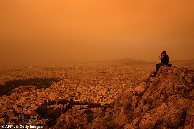 A couple photographed sitting on Tourkovounia Hill, as southerly winds carried waves of Saharan dust.  However, the Mars-type filter will be short-lived and skies are expected to clear on Wednesday as winds change.