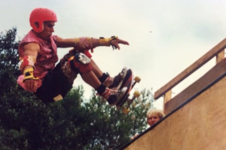 A man wearing a red helmet rides a skateboard up a wooden ramp.