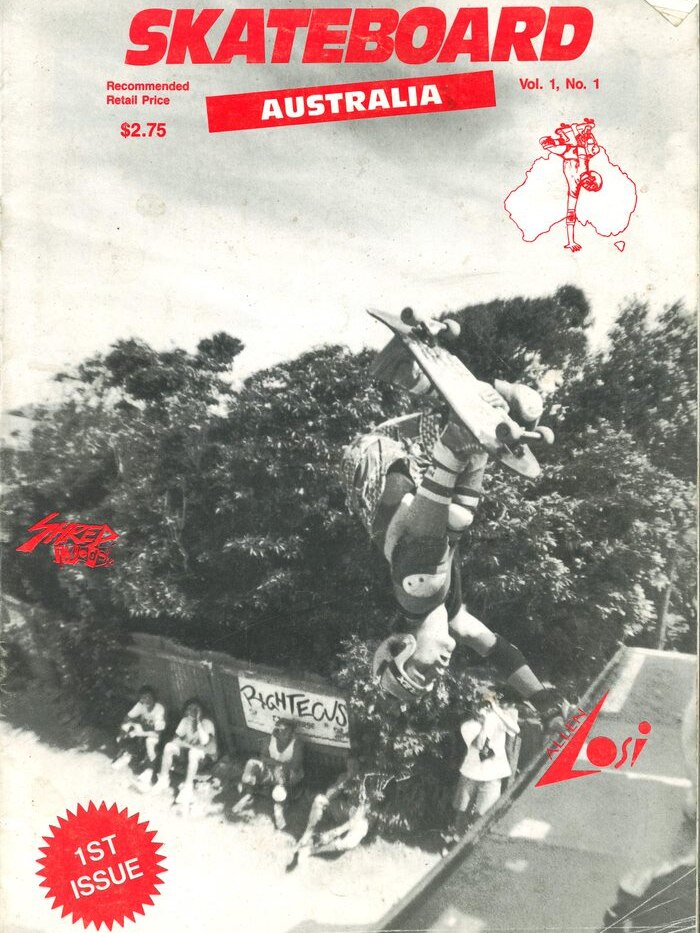A black and white magazine photo of a skateboarder doing a handstand at the top of a skate ramp.