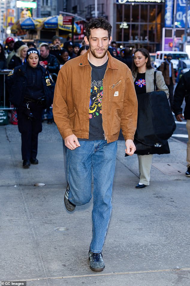 The British actor, 33, wore a brown jacket over a navy T-shirt with a colorful design and blue jeans.