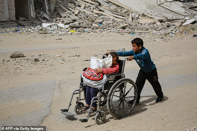 A boy pushes a girl in a wheelchair in front of a destroyed building in Gaza City on March 28.