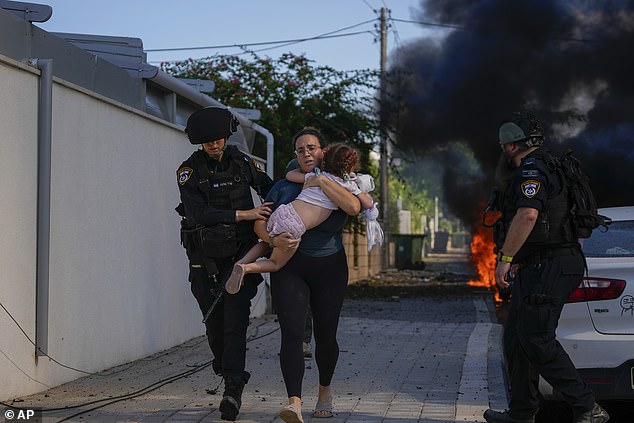 Israeli police officers evacuate a woman and a child from a site hit by a rocket fired from the Gaza Strip, in Ashkelon, southern Israel, Saturday, October 7, 2023.