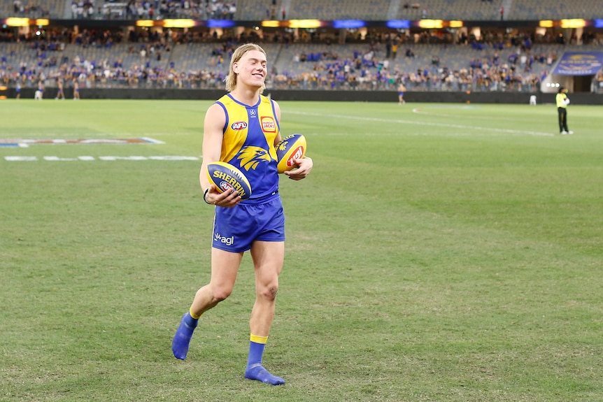 West Coast Eagles player Harley Reid smiles as he carries two footballs after a match.