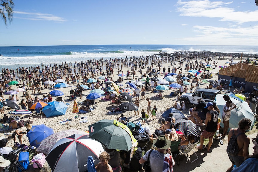 A large crowd on the beach to watch a professional surfing contest.
