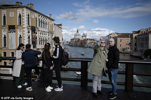 Tourists take selfies with the Grand Canal in the background in the "Academy Bridge" on April 24, 2024 in Venice, on the eve of the start of the official test of the city's reservation system