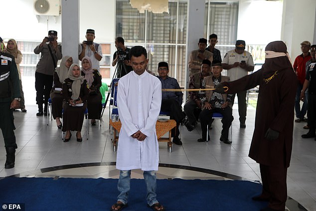 Acehnese man stands firm on blue mat as he receives whipping punishment