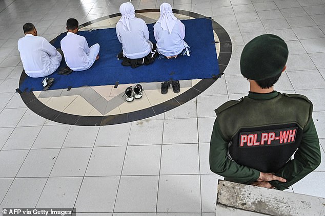 An officer watches over two couples waiting to be flogged by Sharia police as punishment for having forbidden relations with the opposite sex.