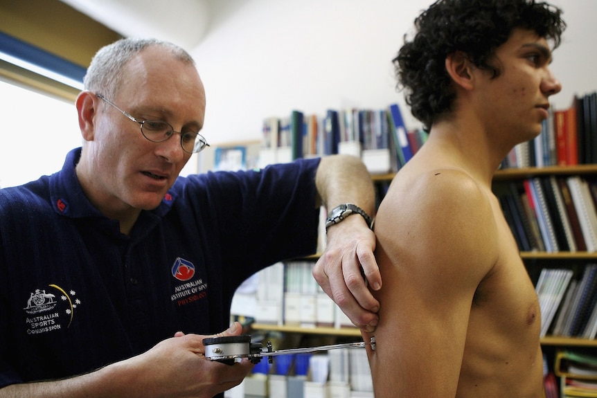 An AFL staff member pinches the back of a player's arm with a skinfold testing instrument.