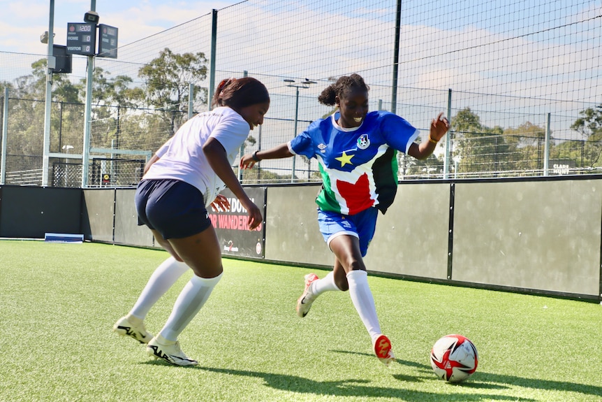 A young African footballer dribbles the ball at an opponent.