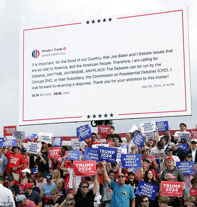 Supporters hold signs as a message is displayed on a large video screen saying that former President Donald Trump will debate President Joe Biden anytime, anywhere, anywhere.