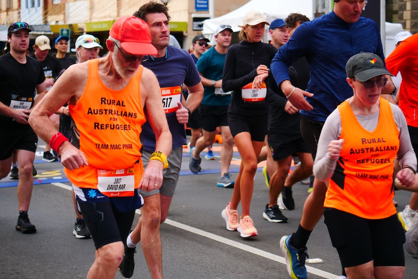An older man in a high-visibility t-shirt running with a group of competitors down a Ballarat street.