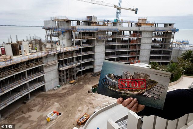 A Grove Isle resident who has been fighting the new condo building under construction holds a pamphlet while standing on an eighth floor balcony.  Stunning views of the bay are now blocked by construction work.