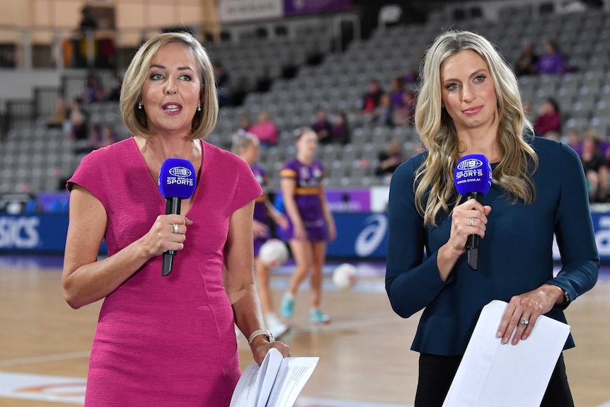 Two netball commentators hold microphones courtside before a Super Netball match.