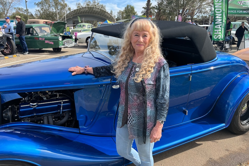 Woman standing with her hand on the hood of a classic electric blue car