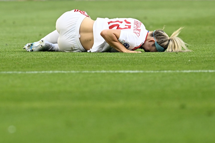 A soccer player lies on the ground after injuring her knee.