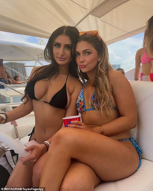 Two women in bikinis are seen posing on one of the many boats while one has her hands on the steering wheel and the other has a red drink in her hand.