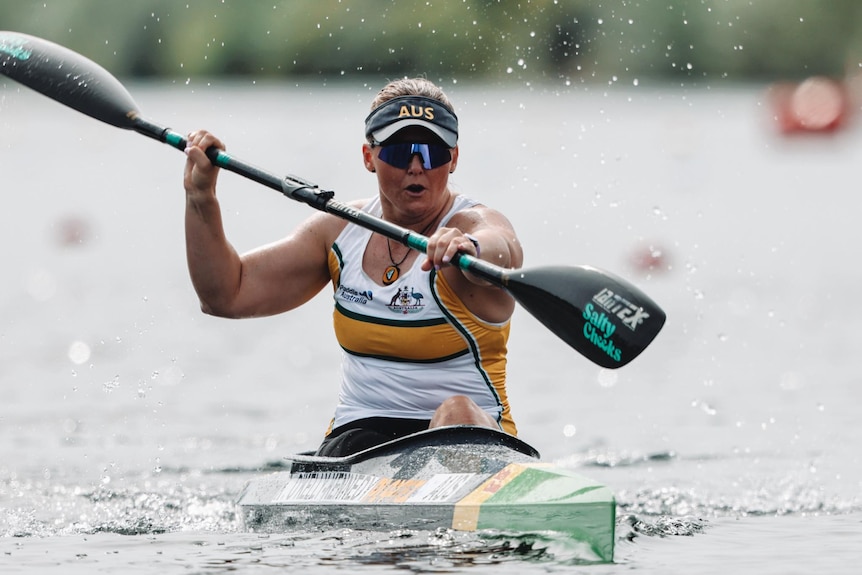 A female kayaker competes in a kayak, with an intense look on her face. 