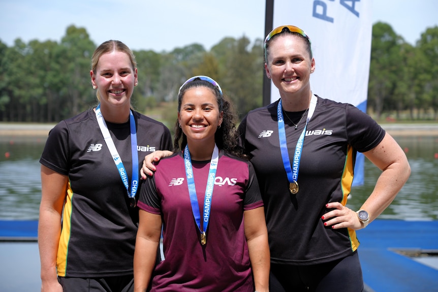 Three paracanoe athletes stand side by side smiling, with medals around their necks.