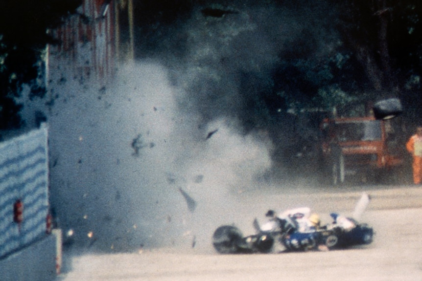 The remains of an F1 car that recently crashed into a wall, with dust, smoke and debris flying into the air.