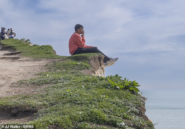 The shocking image shows the man sitting casually smoking a cigarette while on the brink of a 400-foot drop.