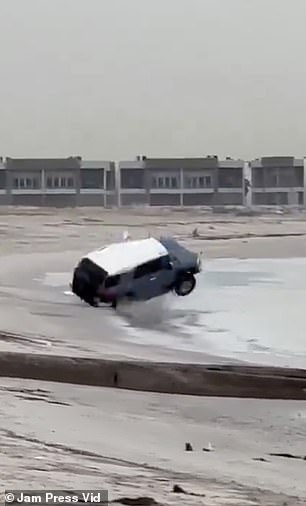 The car swerves before appearing to catch an edge and begins rolling on the sand.
