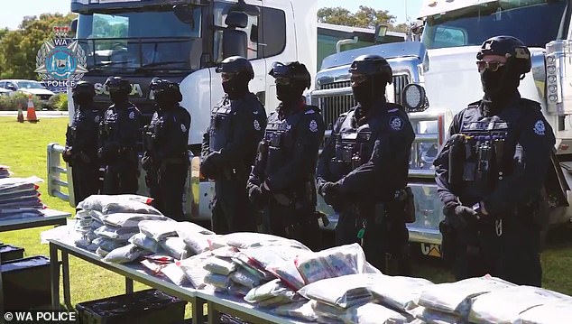 Police officers are seen standing behind a table with millions of dollars seized from a truck.