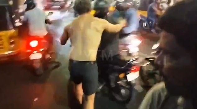 This is the moment a half-naked man lunges at a passing motorcyclist before appearing to bite him.