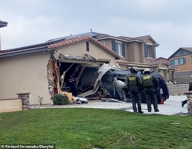Police officers and firefighters are seen assessing the aftermath of the freak accident while the structure of the house is seen hanging and the car stuck on its side.