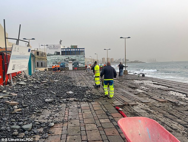 One tourist died and at least 130 people had to be evacuated as Tenerife was hit by freak storms.  Pictured: Workers cleaning up after the storm hit the coast of the Canary Islands.