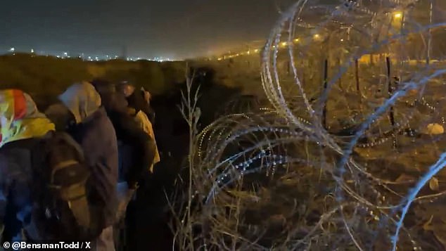 Migrants shelter near the barbed wire fence between Mexico and a border crossing near El Paso, Texas, while Texas law enforcement and the National Guard stand watch on the other side.