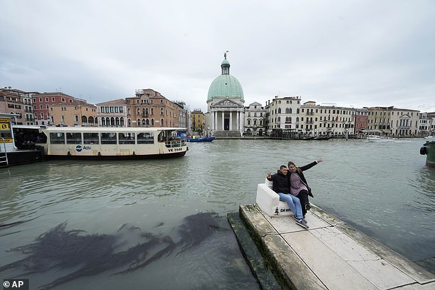 Tourists are pictured sitting on an abandoned couch on a pier in Venice, Italy, Wednesday, April 24, 2024.
