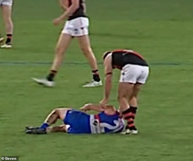 Western Bulldogs star Tom Liberatore falls to the Marvel Stadium turf, where he is assisted by Essendon player Darcy Parish.