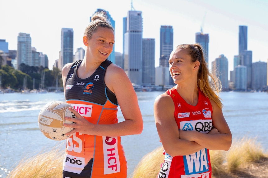 Jo Harten stands tall, holding the Grand Final ball and smiling back to back to Paige Hadley, in front of the Brisbane skyline.
