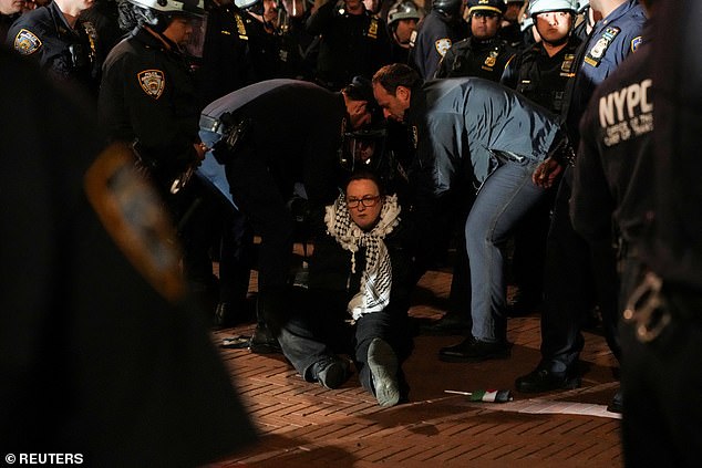 NYPS officers are seen arresting a female protester sitting on the ground with a keffiyeh around her neck.