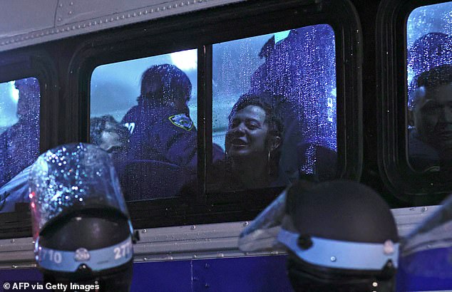 A protester is seen through the rainy window of an NYPD bus as officers take him on after clearing him from the school building.