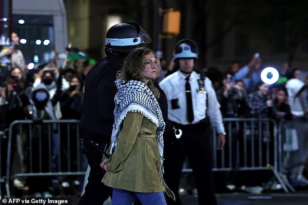 Another protester is seen with her hands behind her back and a keffiyeh around her neck as an officer escorts her.