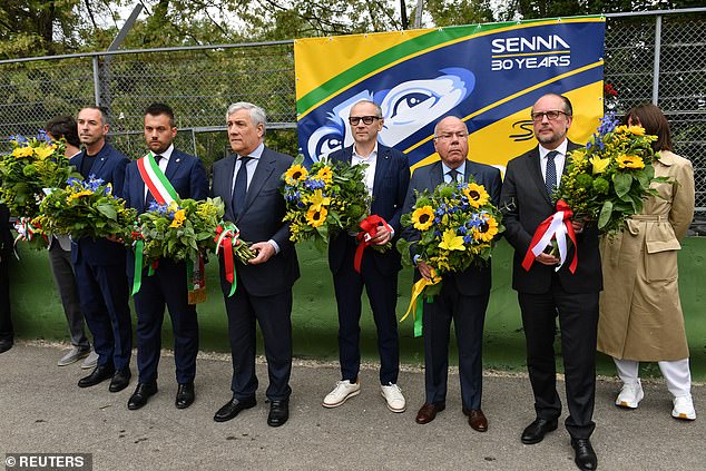 The foreign ministers of Brazil, Austria and Italy pose with Domenicalli in front of a banner with flowers at the exact site of the accident that killed Senna.
