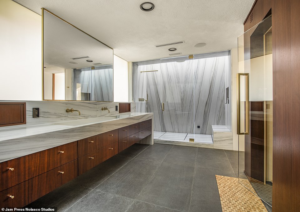 The marble shower is elegant with gold accents and the bathroom features floating wood cabinets.