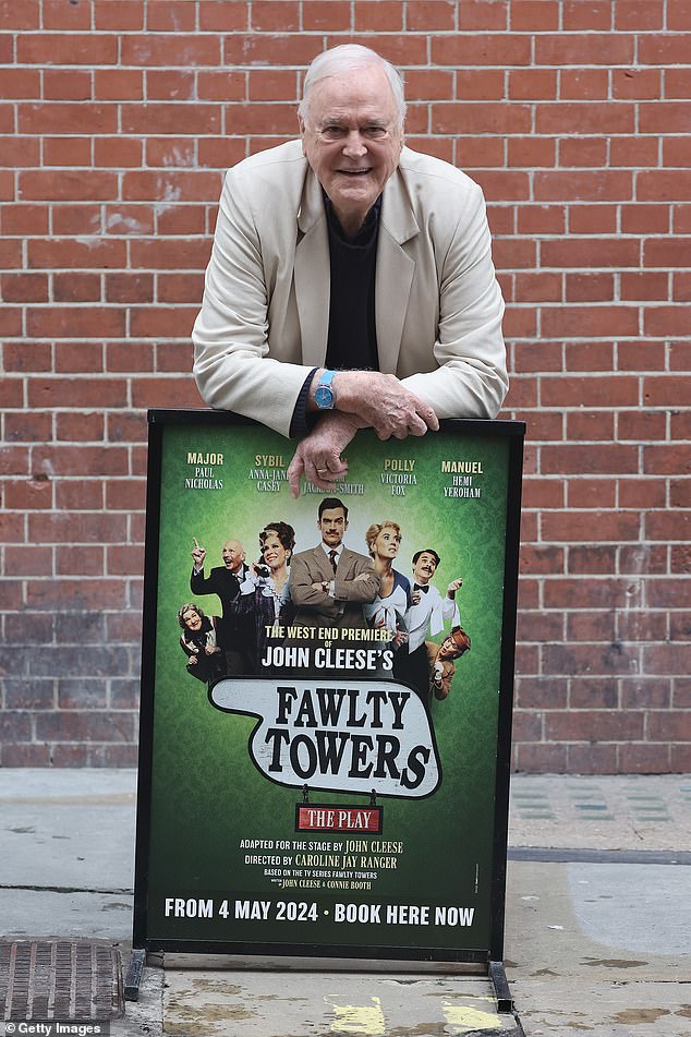 Cleese posing with a poster of his new play that he has adapted to the stage