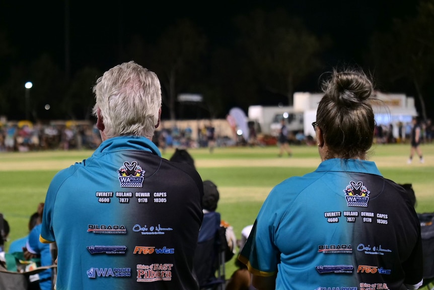 Two people behind wearing light blue sports shirts while watching a rugby match.