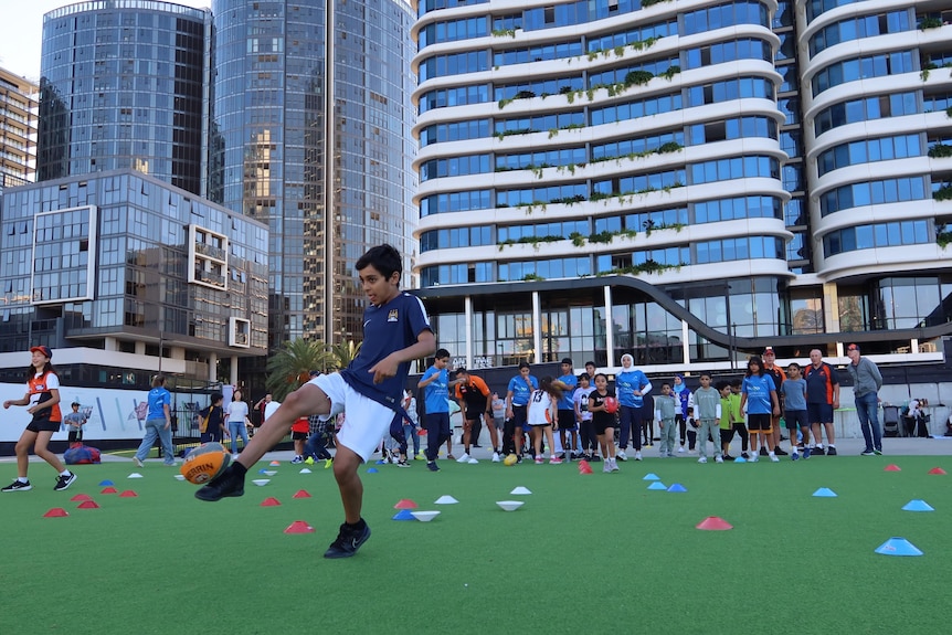 A boy kicks an AFL ball, with a huge building in the background.