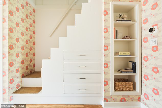 At the end of a wallpapered hallway with built-in storage are steps leading to a renovated attic.