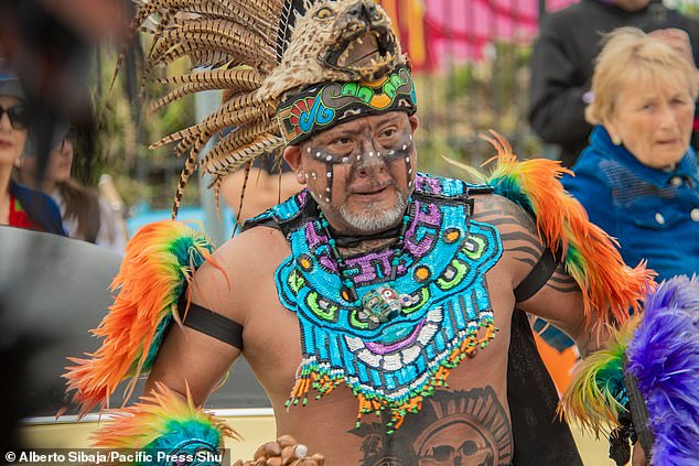 A man was seen wearing a feather piece on his head while dancing with sparkly body paint on his chest and jewelry.