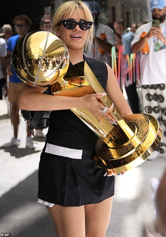 Camila Cabello holds the Larry O'Brien NBA championship trophy in a black and white dress