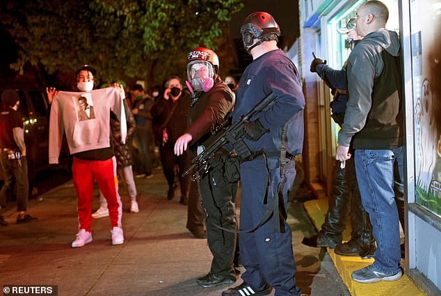 Image from a night of protests and riots in Portland on Oct. 31, 2020. Armed counterprotesters stand outside a bail bond agency as a protester holds up a T-shirt with a photo of black man Kevin E. Peterson Jr., who was murdered at shot by police in vancouver