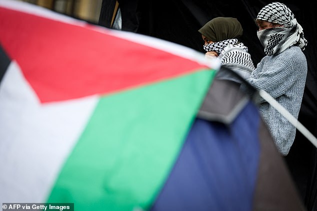 Pro-Palestinian supporters with their faces covered by a keffiyeh stand behind a Palestinian flag at Oxford University in Oxford, eastern England, on May 7, 2024.