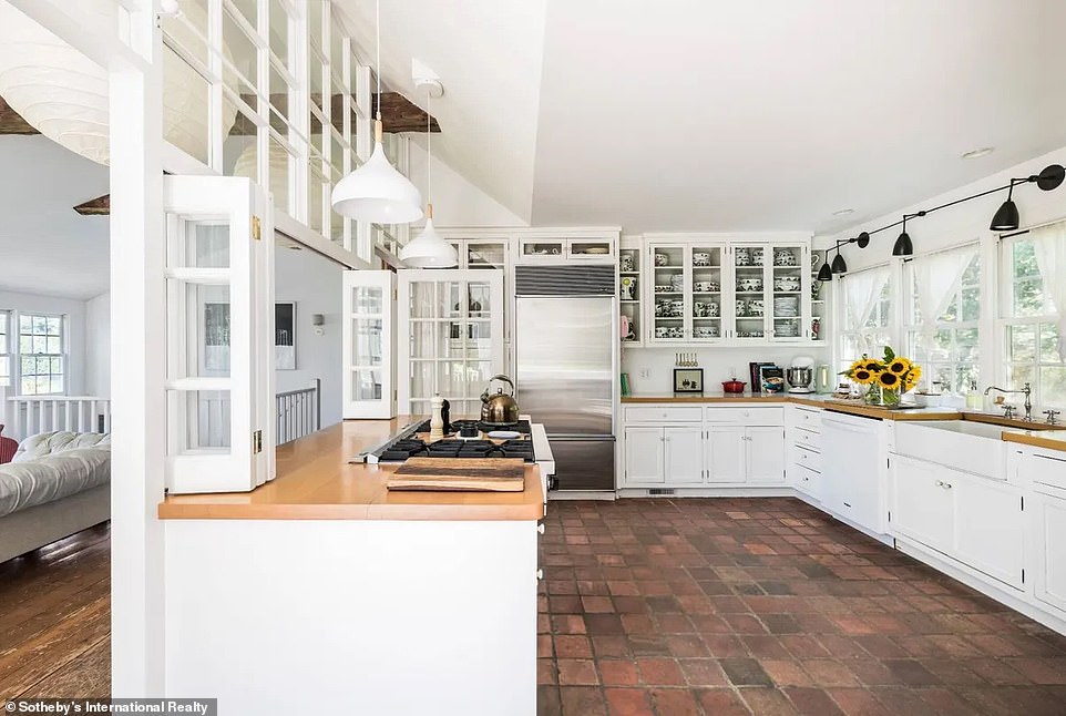 The kitchen features tile floors, a row of windows over the sink offering views of the outside foliage, and a wood-topped breakfast bar.