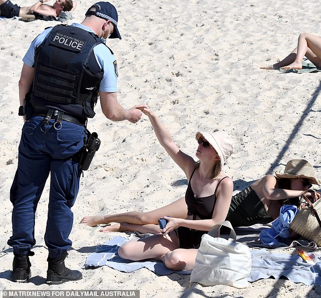 A masked police officer checks a woman's ID on Bondi beach in 2021